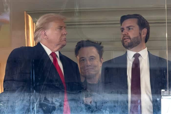 Elon Musk stands behind Donald Trump and JD Vance.
