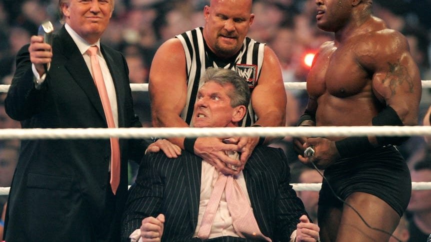 Trump holds up a hair razor over the head of a man being held by two min in a wrestling ring