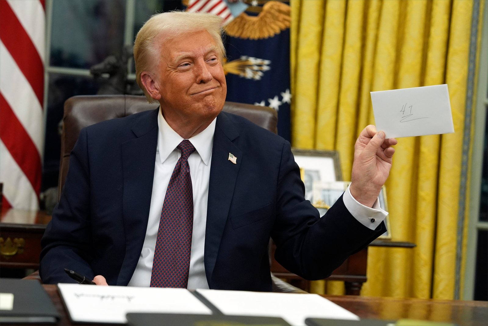 President Donald Trump in the Oval Office holding up a letter from President Biden.