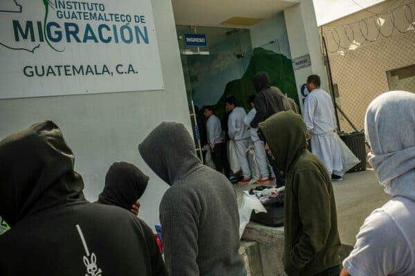 People, mostly in hoodies, enter a space with a sign reading “Migracion, Guatemala, C.A.”
