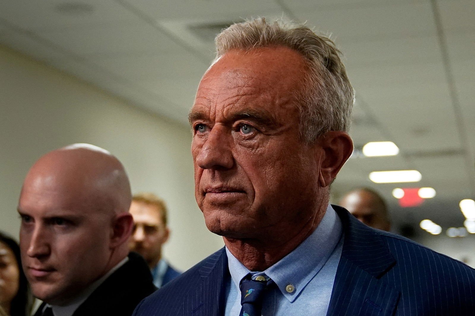 Robert F Kennedy Jr walks through a hallway with a blank expression
