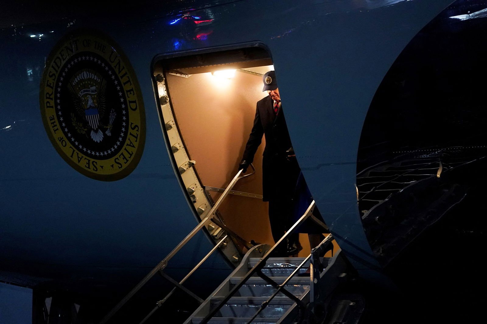 Joe Biden descends the stairs of Air Force One, wearing a navy baseball cap
