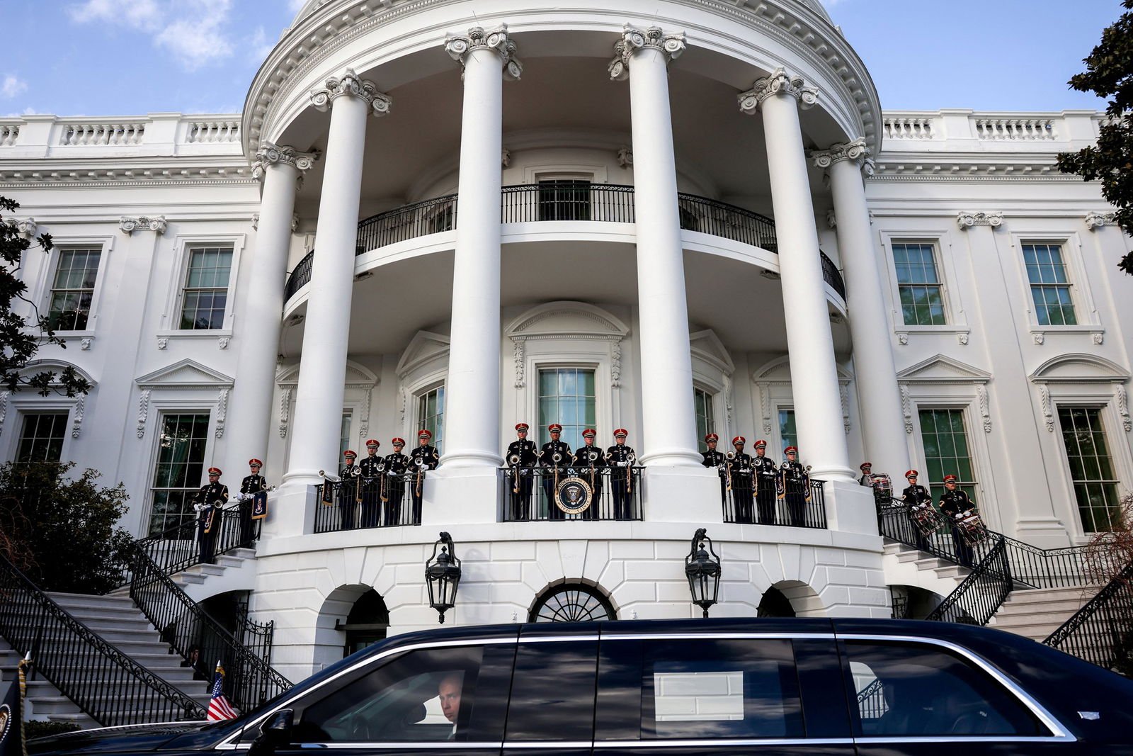 A town car sits at the front of the White House as staff line the front entry