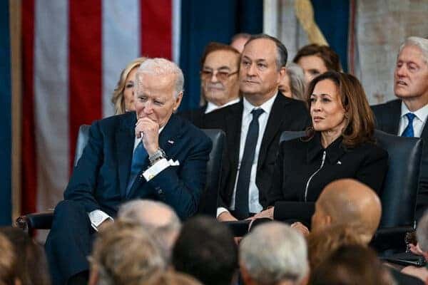 A group of people watching the inauguration ceremony. Joe Biden and Kamala Harris are in the front row. Their spouses are behind them. Bill Clinton is over Ms. Harris’s left shoulder.