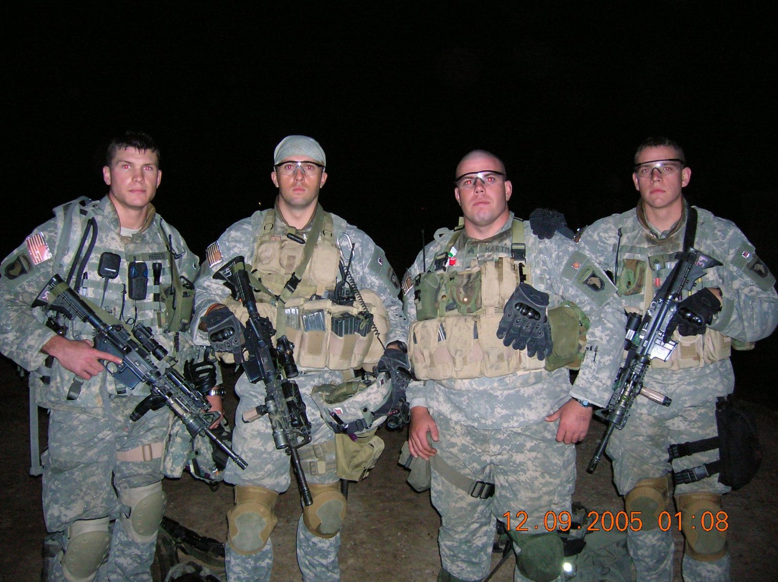 Four soldiers in camouflage uniforms and tactical gear pose at night.