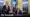 Two men are in an office with a large desk and yellow curtains. One is seated, gesturing with his hands, while the other stands beside him holding a folder. The room has the American and presidential flags, hinting at Trump-era decor. The Telegraph logo is in the corner.
