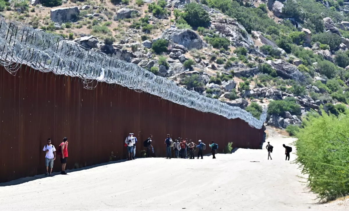 Migrants walk into the U.S. beside the US-Mexico border wall at Jacumba Hot Springs, California, on June 5, 2024.